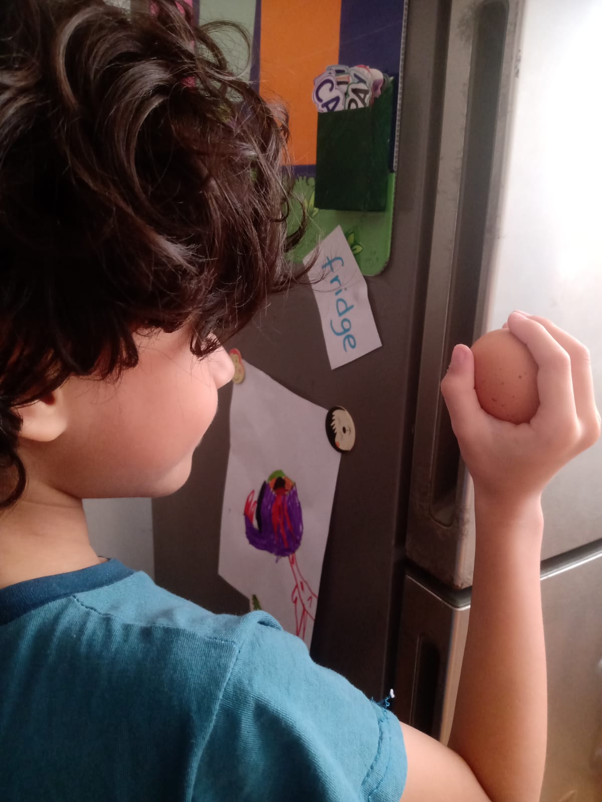 Enzo de perfil junto al refrigerador, sosteniendo el segundo huevo con concentración, listo para intentarlo de nuevo